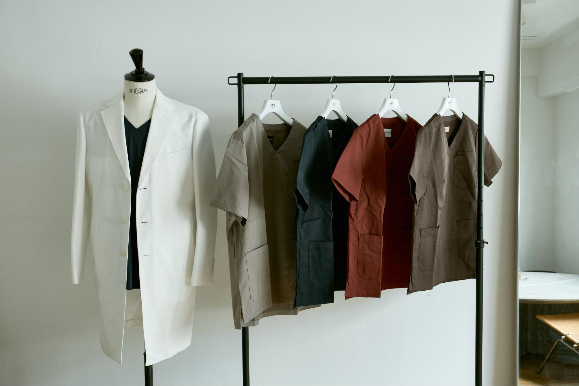 グレー、ネイビー、ボルドー、ブラウンのクリニック制服と白衣がハンガーにかかっている